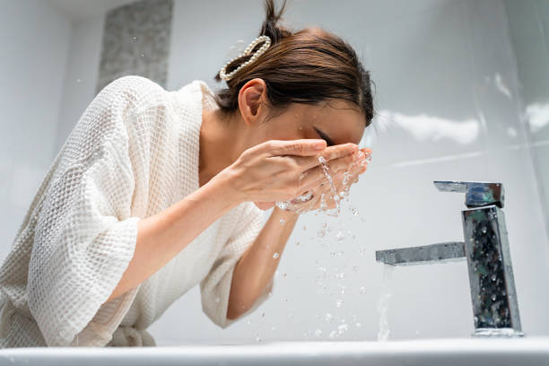 Woman washing face with water in bathroom sink