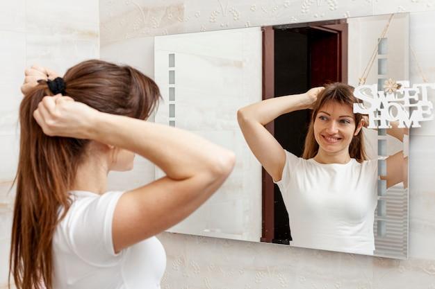 Smiling woman tying her hair in mirror