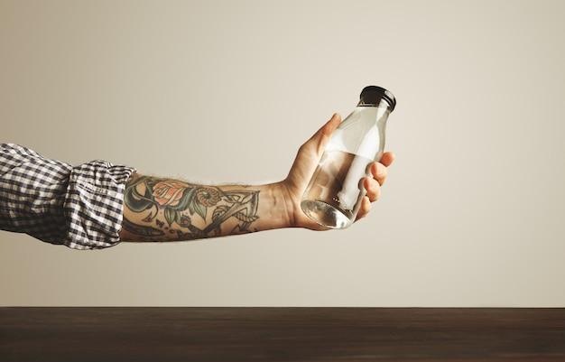 Person holding a clear glass bottle with tattooed arm